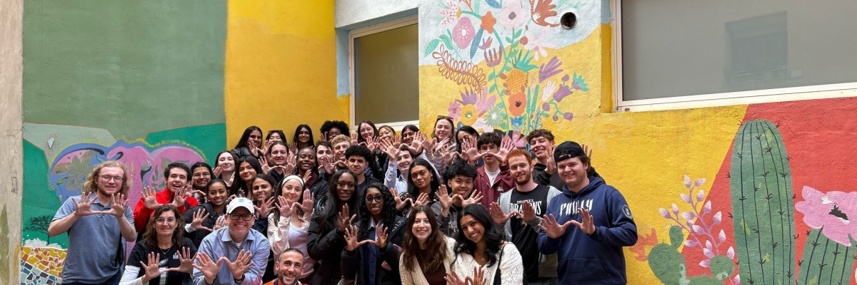 Gruppe af unge VITA Explorers, der deltager i et lokalt fællesskabsprojekt, foran en farverig vægmaleri med blomster og kaktusser.