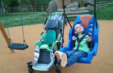 Smilende barn med multiple handicap i en tilpasset gynge i en inkluderende park